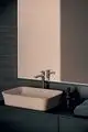 Ideal Standard Waschbecken mit moderner Chromarmatur, rechteckigem Becken in sanften Farben, platziert auf einer dunklen Holzoberfläche vor einem minimalistisch gerahmten Spiegel.